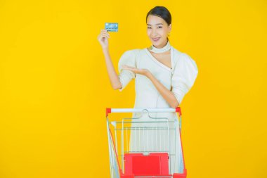 Renkli arka planda süpermarketten alınmış market sepetiyle gülümseyen güzel Asyalı kadın portresi.