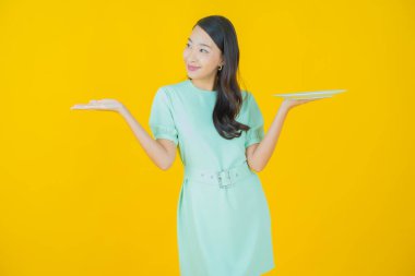 Güzel Asyalı bir kadının portresi. Arka planda boş tabak tabağıyla gülümsüyor.