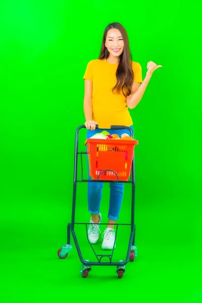 穿着绿色背景的超市购物篮和购物车的美丽的亚洲年轻女子的画像 — 图库照片