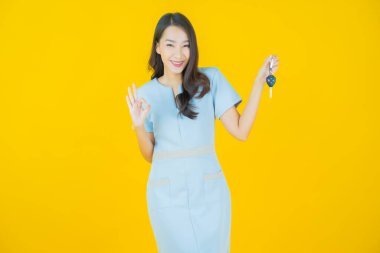 Asyalı güzel bir kadının portresi. Sarı arka planda araba anahtarıyla gülümsüyor.