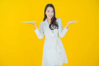 Güzel Asyalı bir kadının portresi. Arka planda boş tabak tabağıyla gülümsüyor.