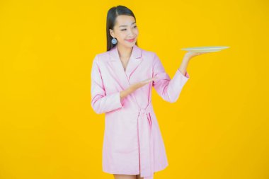 Güzel Asyalı bir kadının portresi. Arka planda boş tabak tabağıyla gülümsüyor.