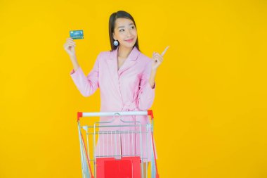 Renkli arka planda süpermarketten alınmış market sepetiyle gülümseyen güzel Asyalı kadın portresi.