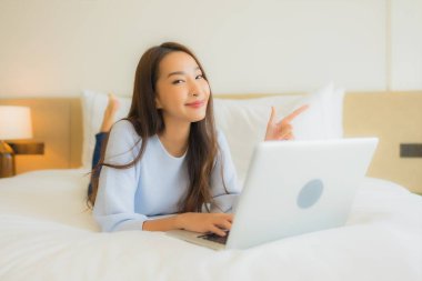 Güzel bir Asyalı kadın yatak odasının iç kısmında bilgisayar kullanıyor.