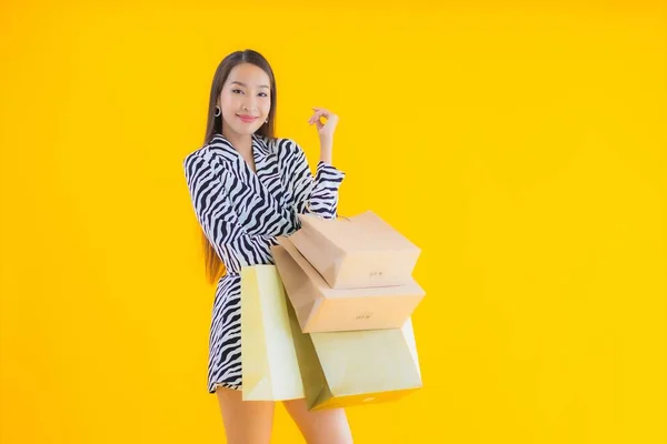 黄色の隔離された背景に小売やデパートからのショッピングバッグと肖像画の美しい若いアジアの女性 — ストック写真