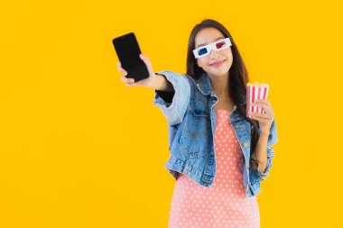 Güzel bir Asyalı kadın portresi telefon patlamış mısırı ve sarı izole edilmiş bir arka planda film izlemekten memnun.