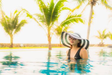 Güzel bir Asyalı kadın portresi, gün batımında palmiye ağacıyla birlikte havuz kenarında dinleniyor ya da tatil için gün doğumunda dinleniyor.