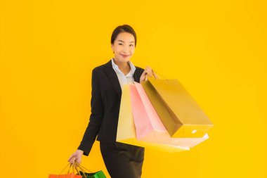 Sarı izole edilmiş arka planda alışveriş merkezinden alışveriş çantasıyla güzel bir genç Asyalı kadın portresi.