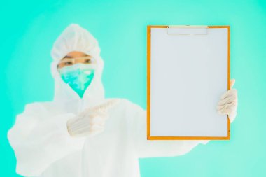 Güzel, genç Asyalı doktor kadın koronavirüsten korunmak için ppe ya da kişisel koruyucu ekipman takıyor ya da mavi izole arka planda beyaz kartı olan 19. bölgede yaşıyor.