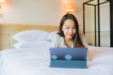 Güzel bir Asyalı kadının portresi yatak odasının içinde kredi kartıyla tablet kullanıyor.