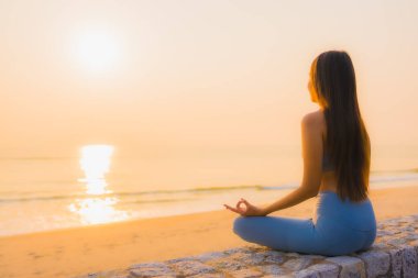 Genç Asyalı kadının portresi sağlık için gün doğumunda deniz kıyısı okyanusunda meditasyon yapıyor.