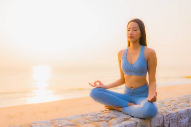 Genç Asyalı kadının portresi sağlık için gün doğumunda deniz kıyısı okyanusunda meditasyon yapıyor.