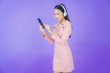 Sarı arka planda müzik dinlemek için kulaklığı ve akıllı telefonu olan güzel Asyalı kadın portresi.