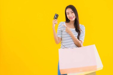 Renkli alışveriş çantası ve sarı izole edilmiş arka planda kredi kartıyla güzel bir Asyalı kadın portresi