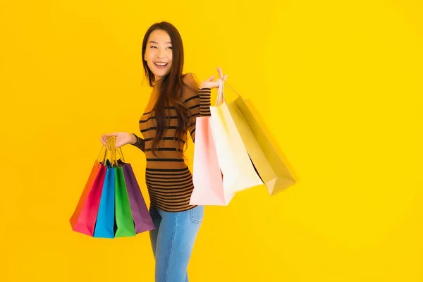 亚洲年轻貌美的女人面带微笑 带着很多色彩的购物袋从百货商店出来 背景是黄色孤立的 — 图库照片