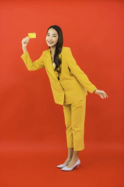 Güzel bir Asyalı kadının portresi kırmızı arka planda kredi kartıyla cep telefonu kullanıyor.