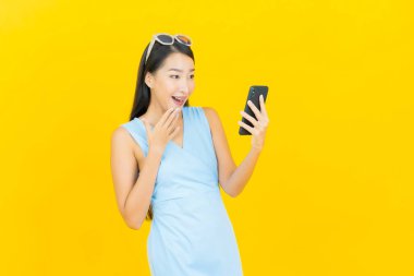 Asyalı güzel bir kadının portresi sarı arka planda akıllı cep telefonuyla gülümsüyor.