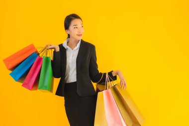 Sarı izole edilmiş arka planda alışveriş merkezinden alışveriş çantasıyla güzel bir genç Asyalı kadın portresi.