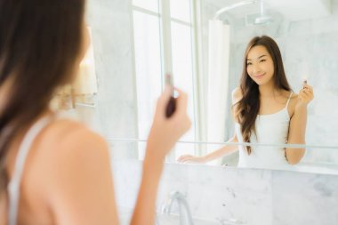 Güzel bir Asyalı kadın portresi. Banyo içerisindeki aynada yüzünü kontrol et ve makyaj yap.