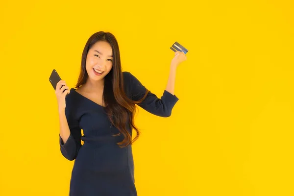 亚洲年轻貌美的女性形象 拥有智能手机 手机和信用卡 背景是黄褐色的 — 图库照片