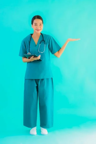 Portrait beautiful young asian doctor woman use smart tablet device on blue isolated background