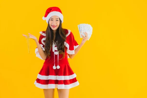 肖像美しい若いアジアの女性が身に着けていますクリスマス服と帽子とともに現金とお金で黄色隔離された背景 — ストック写真