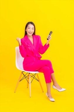 Güzel bir Asyalı kadın portresi sarı renkli izole edilmiş arka planda akıllı cep telefonu kullanır.