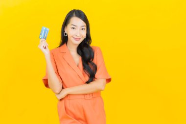 Asyalı güzel bir kadının portresi. Sarı arka planda kredi kartıyla gülümsüyor.