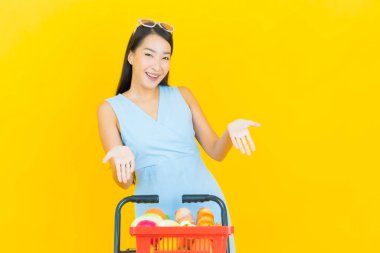 Asyalı güzel bir kadının portresi. Sarı arka planda süpermarketten alınmış alışveriş sepetiyle gülümsüyor.