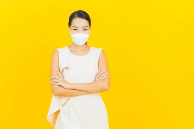 Sarı arka planda Covid19 veya virüsü korumak için maskeli güzel Asyalı kadın portresi