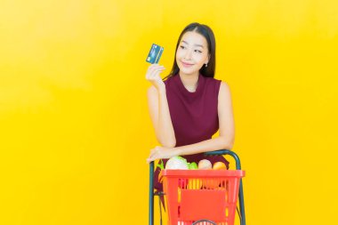 Renkli arka planda süpermarketten alınmış market sepetiyle gülümseyen güzel Asyalı kadın portresi.