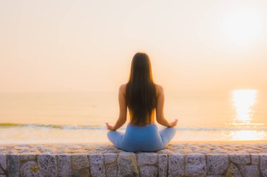 Genç Asyalı kadının portresi sağlık için gün doğumunda deniz kıyısı okyanusunda meditasyon yapıyor.