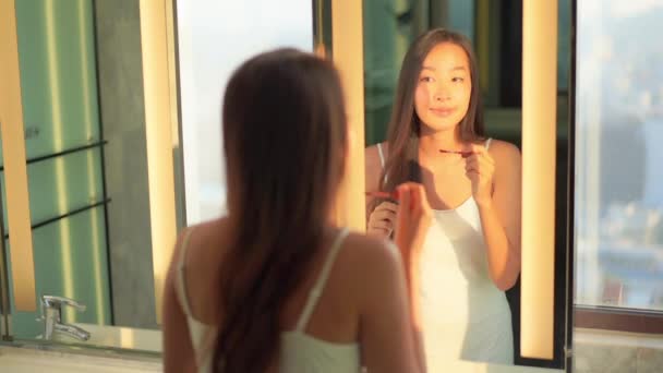 バスルームで鏡を見ながら化粧をしている若いアジア人女性の映像 — ストック動画