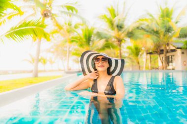 Güzel bir Asyalı kadın portresi, gün batımında palmiye ağacıyla birlikte havuz kenarında dinleniyor ya da tatil için gün doğumunda dinleniyor.