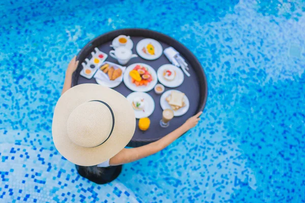 Asyalı güzel bir kadının portresi yüzme havuzunda yüzen kahvaltı tepsisiyle mutlu bir gülümseme