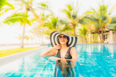 Güzel bir Asyalı kadın portresi, gün batımında palmiye ağacıyla birlikte havuz kenarında dinleniyor ya da tatil için gün doğumunda dinleniyor.