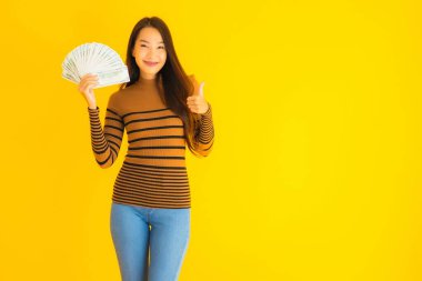 Güzel, genç Asyalı bir kadının portresi mutlu bir gülümseme ve sarı izole edilmiş arka planda bir sürü parası var.