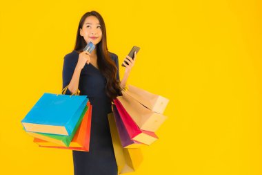 Portre güzel genç Asyalı kadın alışveriş çantası kredi kartı ve akıllı cep telefonu sarısı izole bir arka plan.