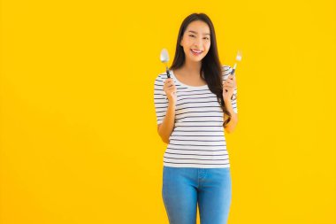 Güzel Asyalı genç bir kadının portresi sarı izole edilmiş arka planda kaşığı ve çatalı yemeye hazır gösteriyor.