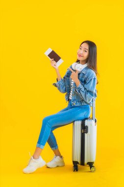 Güzel, Asyalı genç bir kadının portresi valiz ve pasaport ile seyahat, sarı izole arka planda biniş kartı.