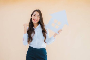 Güzel Asyalı iş kadını portresi izole edilmiş arkaplanda ev işareti ve afişi gösteriyor.