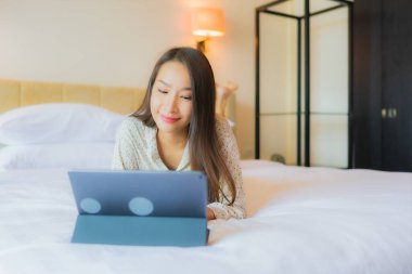 Güzel bir Asyalı kadının portresi yatak odasının içinde kredi kartıyla tablet kullanıyor.