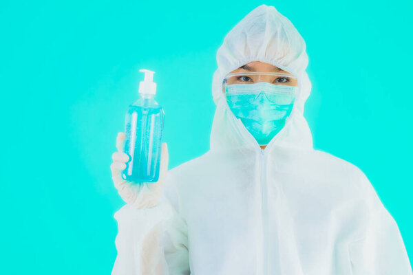 Портрет красивая молодая азиатская врач женщина носить ppe Suite и маску с алкоголем гель на синем изолированном фоне
