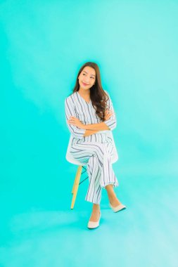 Asyalı güzel bir kadının portresi gülümse ve mavi izole edilmiş arka planda bir sandalyeye otur.