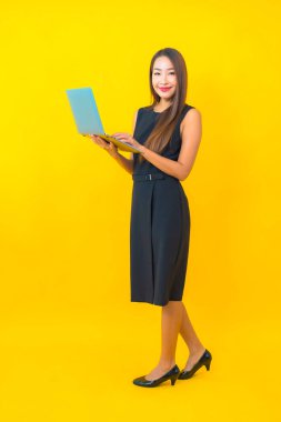 Sarı arka planda dizüstü bilgisayarı olan güzel Asyalı iş kadını portresi