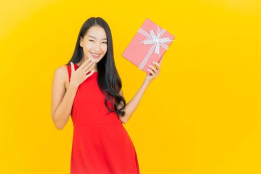 Asyalı güzel bir kadının portresi. Sarı arka planda kırmızı hediye kutusuyla gülümsüyor.