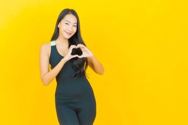 Güzel bir Asyalı kadın, sarı arka planda egzersiz için spor kıyafeti giyer.