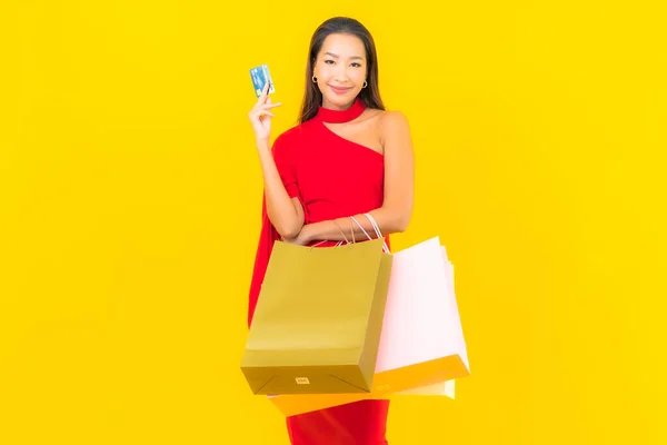 穿着黄色背景的购物袋和信用卡的美丽的年轻亚洲女人的画像 — 图库照片