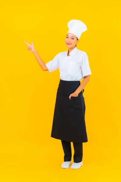 肖像画美しいです若いアジア人女性でシェフまたは調理制服とともに帽子で黄色隔離された背景 — ストック写真
