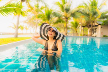 Güzel bir Asyalı kadın portresi, gün batımında palmiye ağacıyla birlikte havuz kenarında dinleniyor ya da tatil için gün doğumunda dinleniyor.